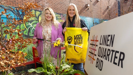 2 ladies with a litter picker and a yellow bag in front of a colourful mural.